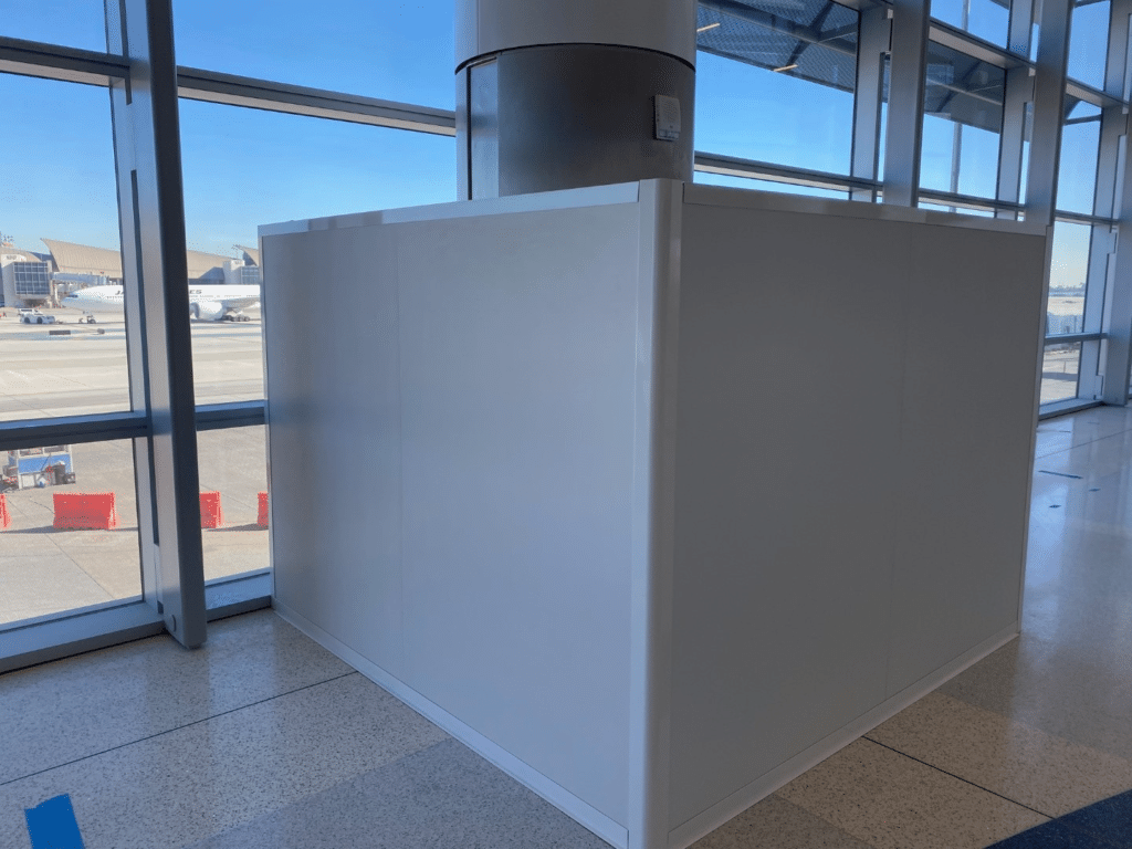 a temporary wall surrounding a large poll in an airport hallway, showing how to reduce construction costs